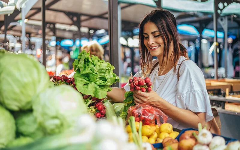 Eine junge Frau kauft auf einem regionalen Markt saisonales Gemüse ein.