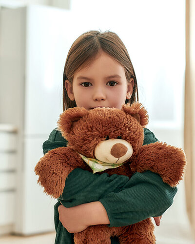 Ein kleines Mädchen drückt seinen Teddybären fest an sich und schaut schüchtern nach vorne.