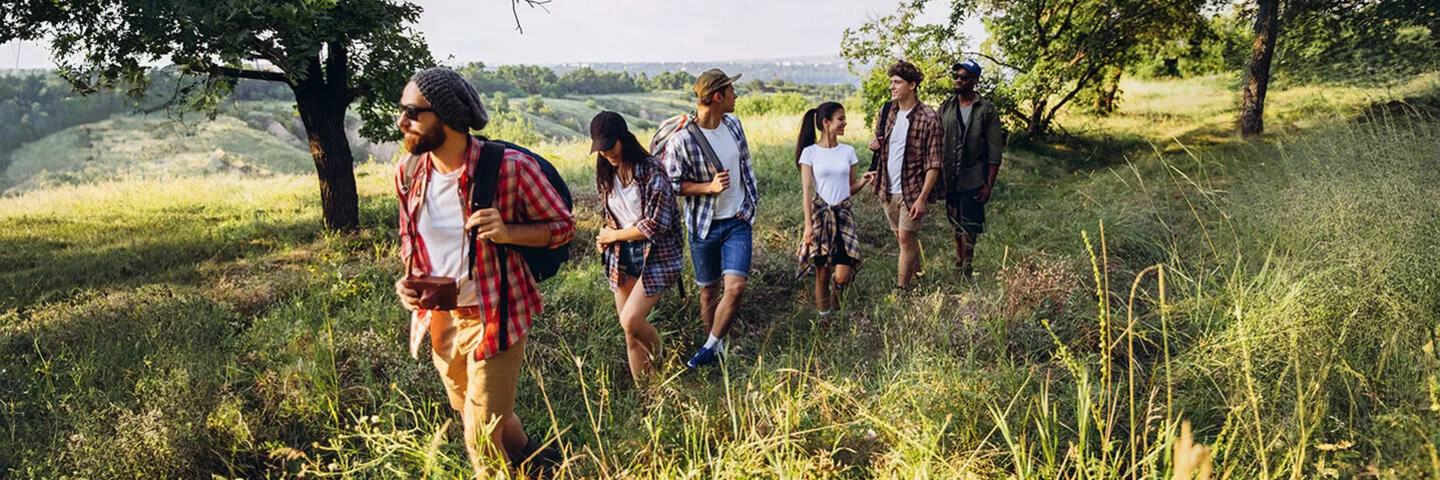Gruppe von jungen Männer und Frauen gehen zusammen unter Bäumenspazieren.
