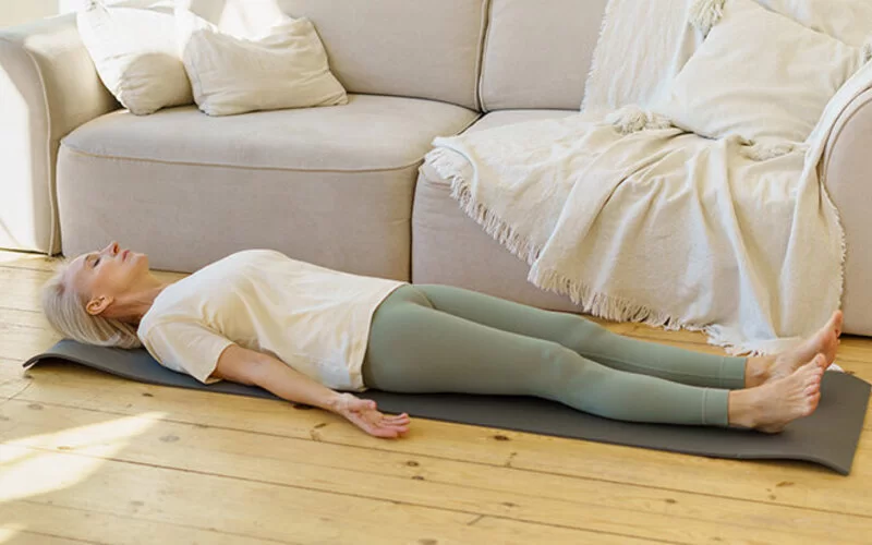 Frau liegt auf dem Boden und wendet eine Entspannungstechnik gegen ihre chronischen Schmerzen an.