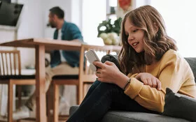 Mädchen sitzt allein auf Couch mit Smartphone in der Hand.