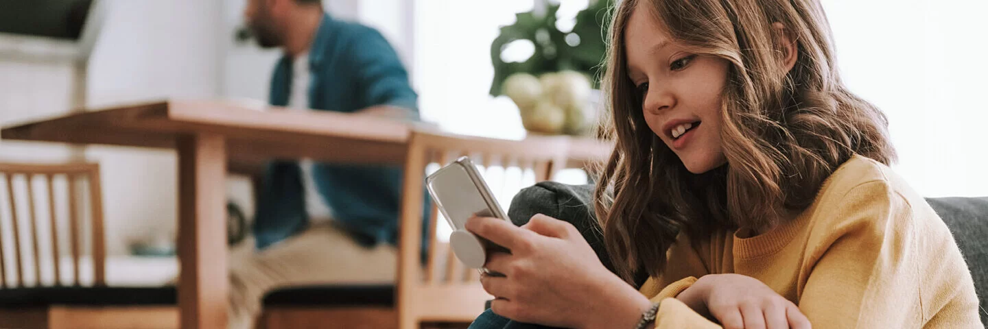 Mädchen sitzt allein auf Couch mit Smartphone in der Hand.