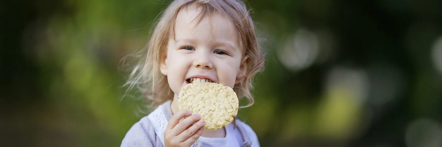 Ein kleines Mädchen beißt in eine Maiswaffel.