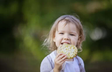 Ein kleines Mädchen beißt in eine Maiswaffel.