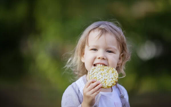 Ein kleines Mädchen beißt in eine Maiswaffel.