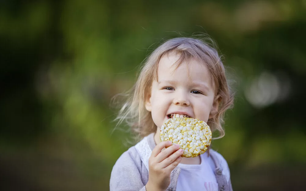 Ein kleines Mädchen beißt in eine Maiswaffel.