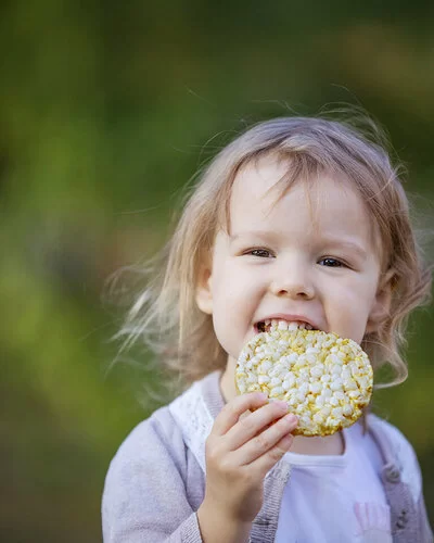 Ein kleines Mädchen beißt in eine Maiswaffel.