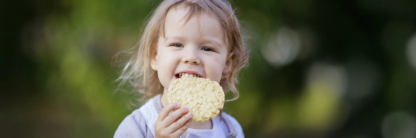 Ein kleines Mädchen beißt in eine Maiswaffel.