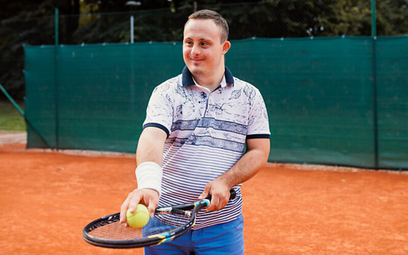 Ein junger Mann mit Behinderung spielt Tennis.