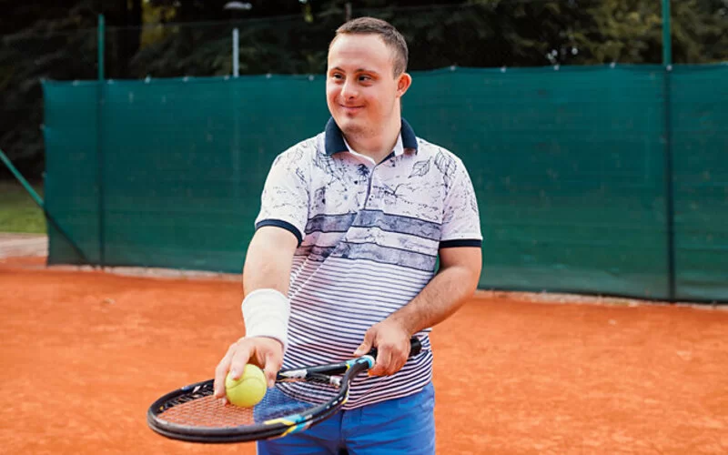 Ein junger Mann mit Behinderung spielt Tennis.