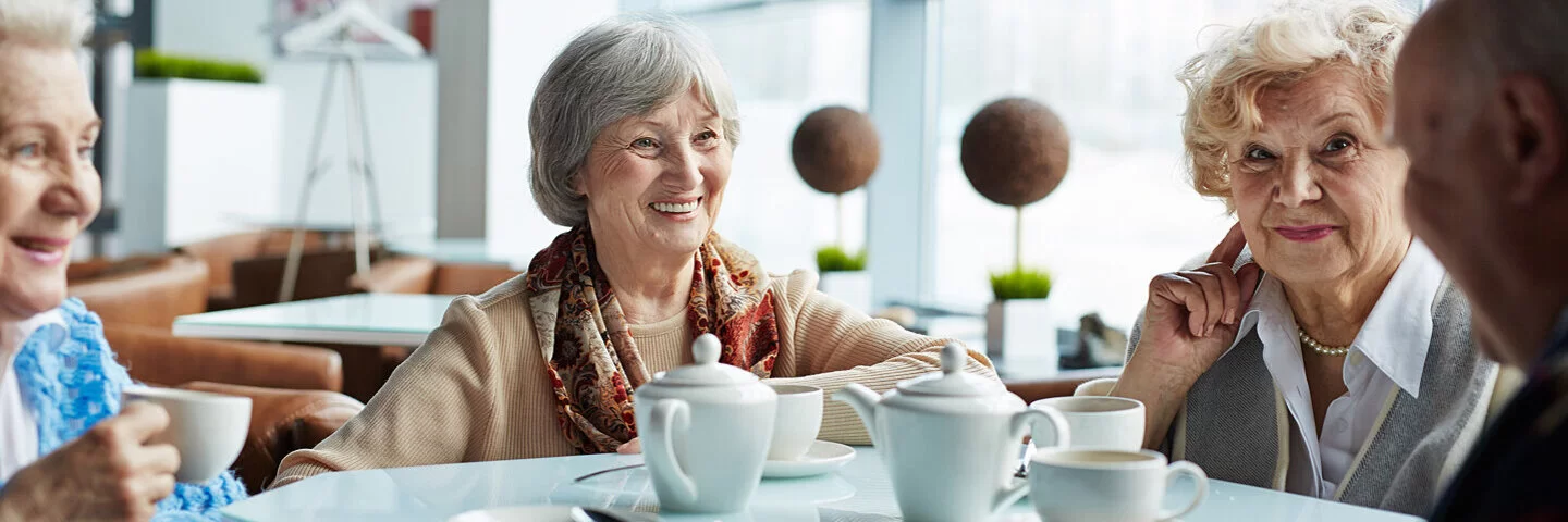 Vier ältere Menschen kennen sich durchs betreute Wohnen – sie sitzen gemeinsam vergnügt im Cafe.