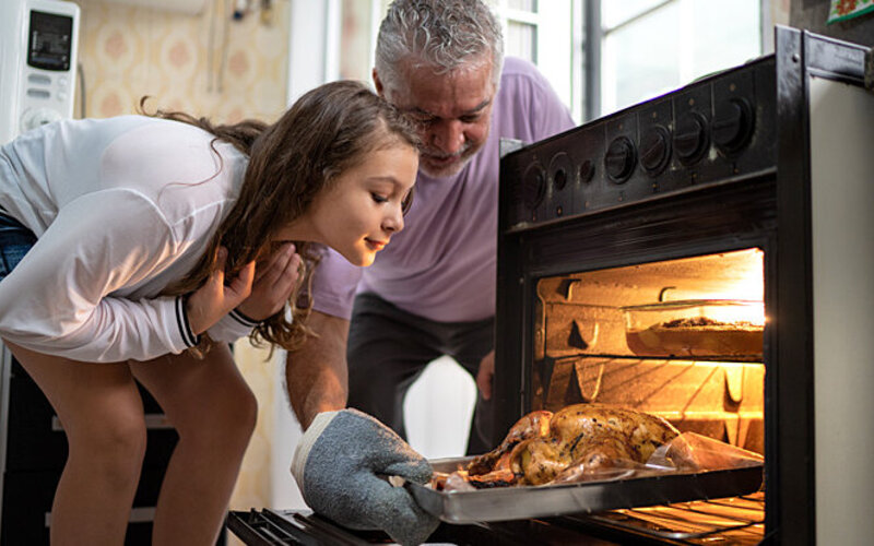 Ein Mädchen und Großvater öffnen den Ofen und schauen sich den Weihnachtsbraten gemeinsam an.