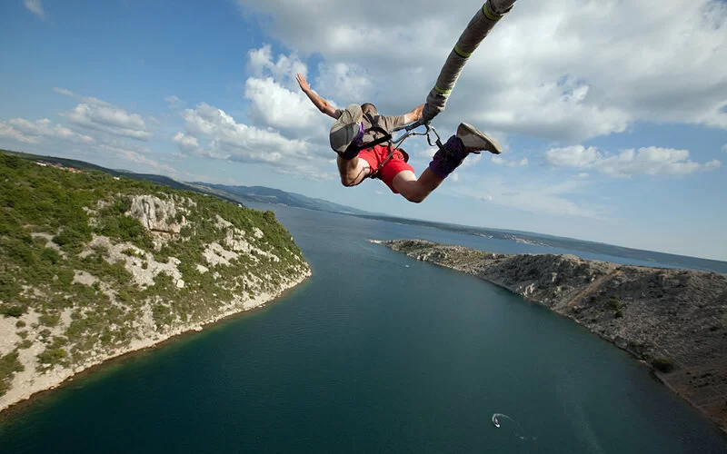 Ein Mann mit Fernweh macht Bungee-Jumping über einem Meeresausläufer.