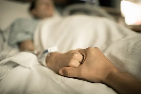 Eine Person hält die Hand einer anderen Person, die in einem Krankenhausbett liegt.