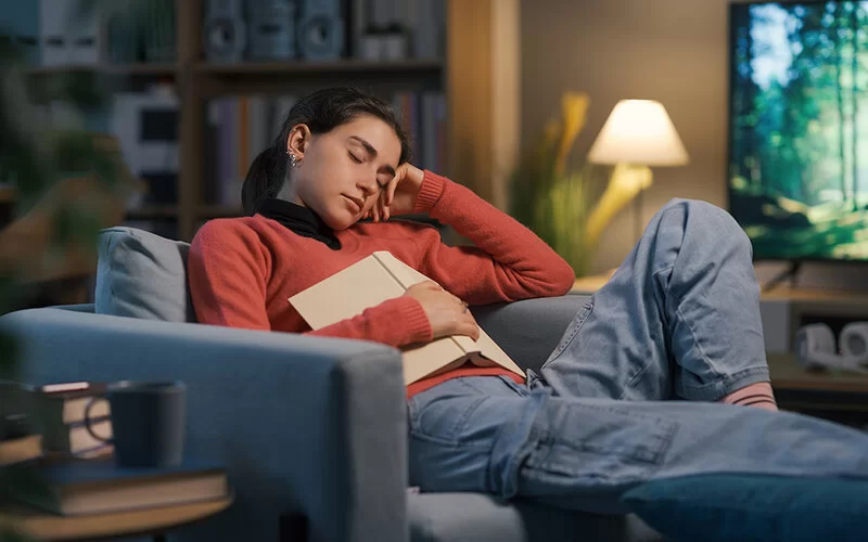 Eine Frau ist mit einem Buch auf dem Sofa eingeschlafen.