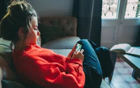 Ein junges Mädchen in einem roten Pullover schaut auf ihr Smartphone.