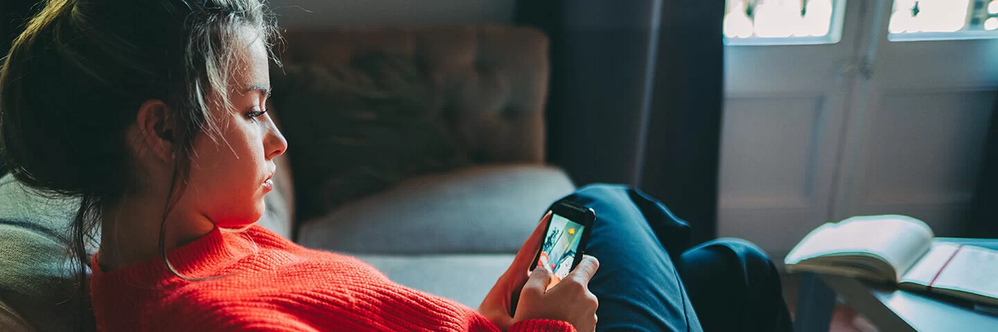 Ein junges Mädchen in einem roten Pullover schaut auf ihr Smartphone.