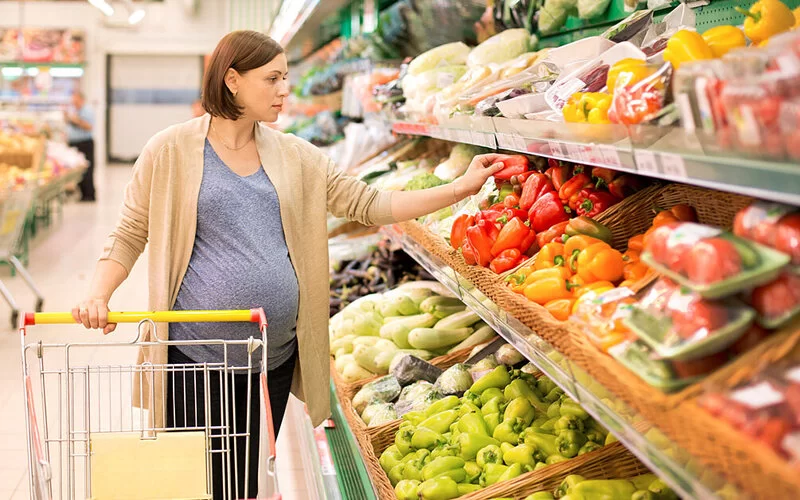 Eine Schwangere kauft in einem Supermarkt Gemüse ein.