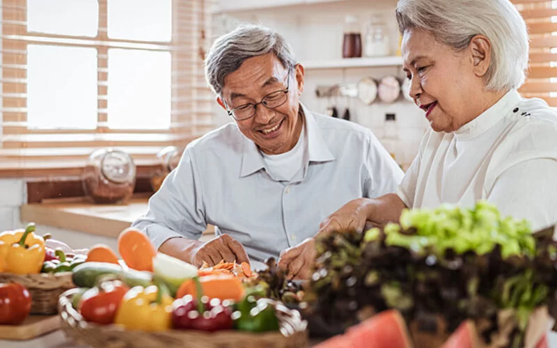Ein älteres Ehepaar, das sich nach der DASH-Diät ernährt, steht am Küchentresen und bereitet Speisen zu.