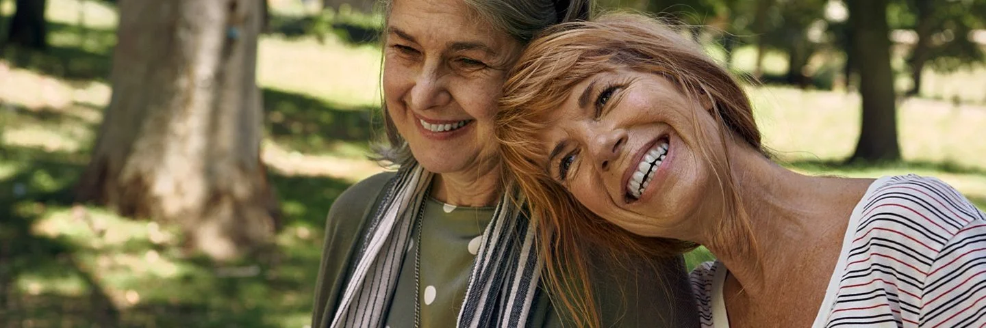 Zwei Frauen mit glücklichem Gesichtsausdruck gehen draußen spazieren. Es gibt Möglichkeiten, einer Depression vorzubeugen.