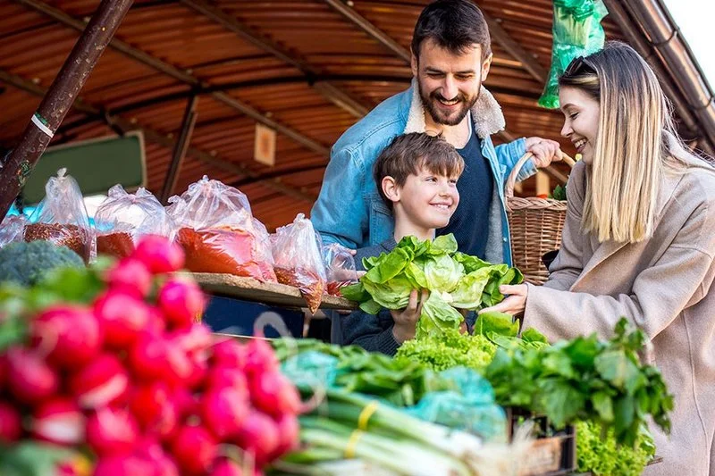Eine Familie mit Kind kauft frisches Gemüse an einem Marktstand