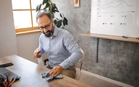 Mann hält Hygiene am Arbeitsplatz, indem er den Schreibtisch wischt.