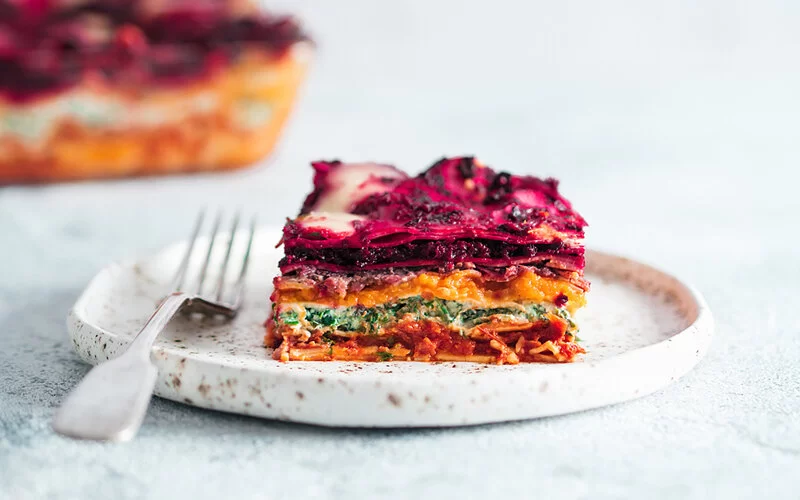 Auf einem hellen Teller ist ein Stück bunte Lasagne mit gesunder Roter Bete angerichtet.