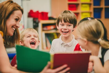 Eine Frau zeigt Kindern ein geöffnetes Buch. Sie lachen freudig über das, was sie in dem Buch sehen.