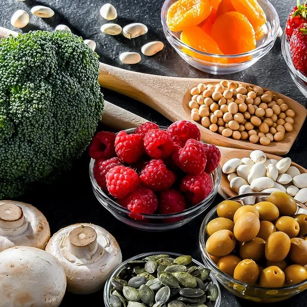 Auf einem Tisch sind verschiedene frische Lebensmittel wie Brokkoli, Beeren, Nüsse, Haferflocken und Fleisch arrangiert.