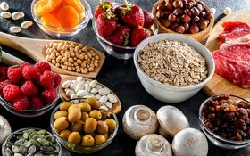 Auf einem Tisch sind verschiedene frische Lebensmittel wie Brokkoli, Beeren, Nüsse, Haferflocken und Fleisch arrangiert.