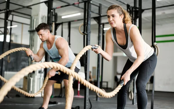 Eine Frau und ein Mann trainieren im Fitnessstudio mit Seilen.