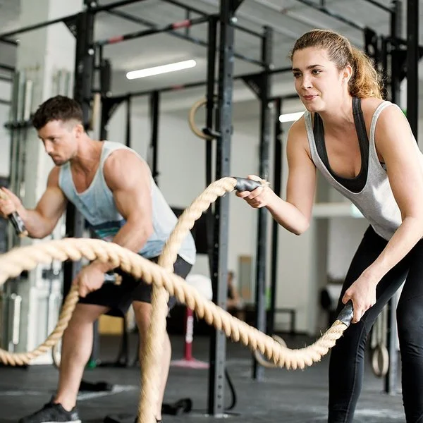 Eine Frau und ein Mann trainieren im Fitnessstudio mit Seilen.