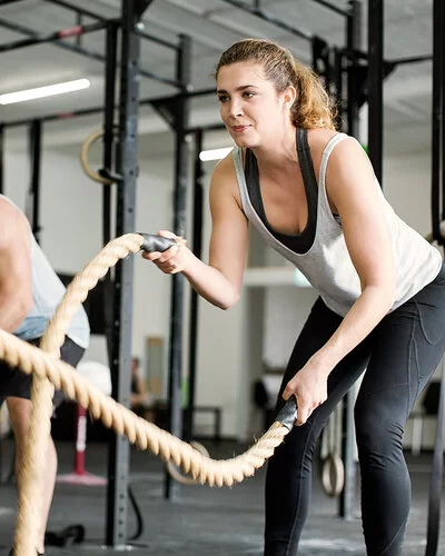 Eine Frau und ein Mann trainieren im Fitnessstudio mit Seilen.
