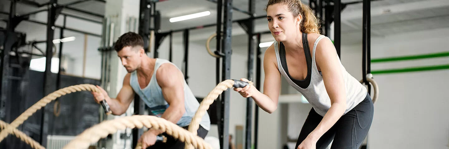 Eine Frau und ein Mann trainieren im Fitnessstudio mit Seilen.