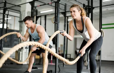Eine Frau und ein Mann trainieren im Fitnessstudio mit Seilen.