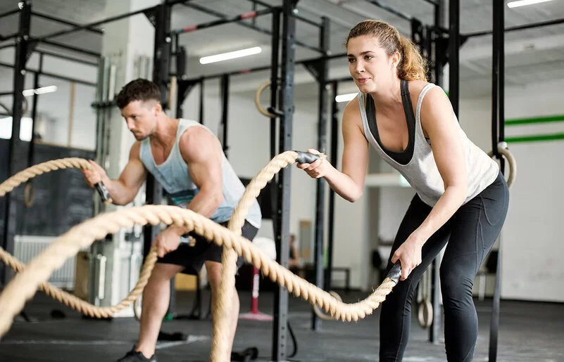 Eine Frau und ein Mann trainieren im Fitnessstudio mit Seilen.
