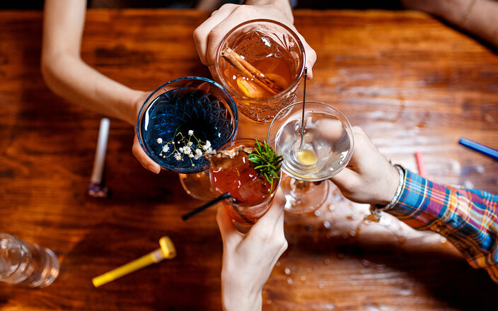 Vier Freunde stoßen mit farbenfrohen Cocktails am Tisch an.