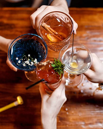 Vier Freunde stoßen mit farbenfrohen Cocktails am Tisch an.