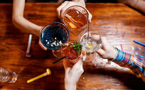 Vier Freunde stoßen mit farbenfrohen Cocktails am Tisch an.
