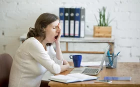 Frau sitzt am Schreibtisch und gähnt.