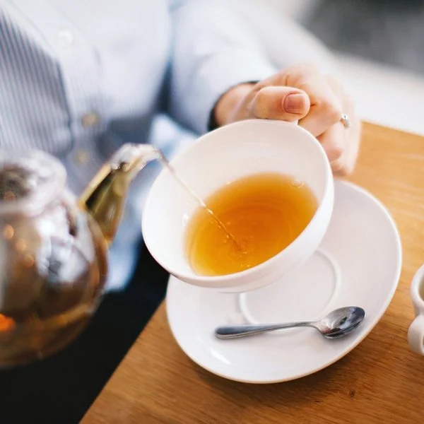 Eine Person gießt sich aus einer Kanne Tee in einer Tasse.
