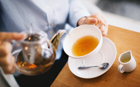 Eine Person gießt sich aus einer Kanne Tee in einer Tasse.