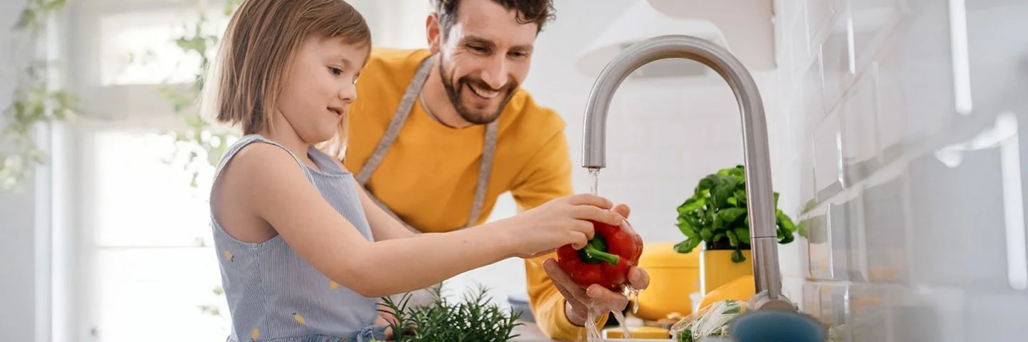 Vater und Tochter waschen gemeinsam frisches Gemüse ab.