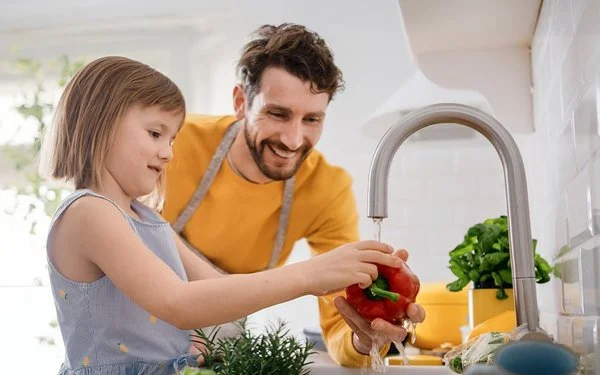 Vater und Tochter waschen gemeinsam frisches Gemüse ab.