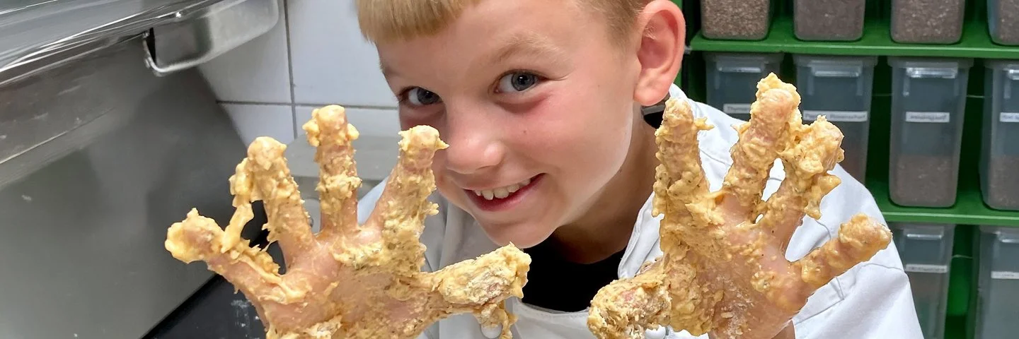 Blonder Junge hält seine vom Teig klebrigen Finger in die Kamera.
