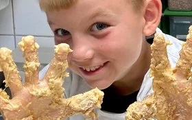 Blonder Junge hält seine vom Teig klebrigen Finger in die Kamera.