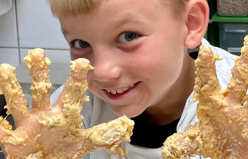 Blonder Junge hält seine vom Teig klebrigen Finger in die Kamera.