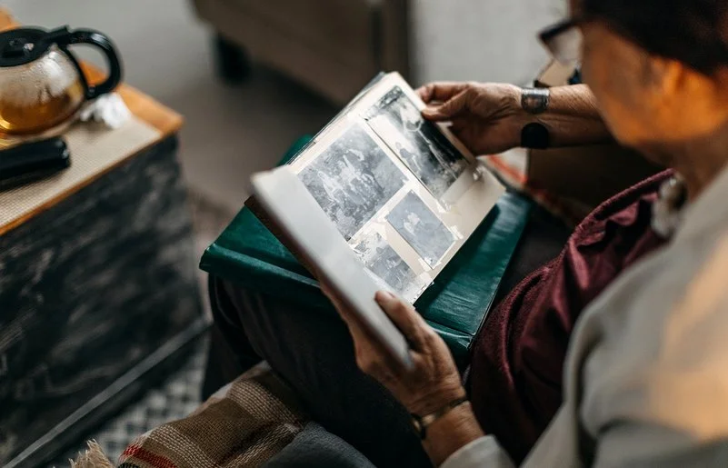 Eine ältere Frau schaut sich alte Schwarz-Weiß-Fotos in einem Fotoalbum an.