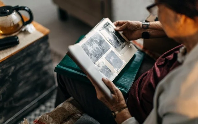 Eine ältere Frau schaut sich alte Schwarz-Weiß-Fotos in einem Fotoalbum an.