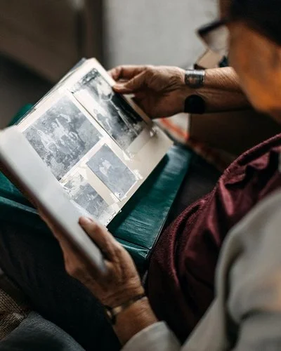 Eine ältere Frau schaut sich alte Schwarz-Weiß-Fotos in einem Fotoalbum an.